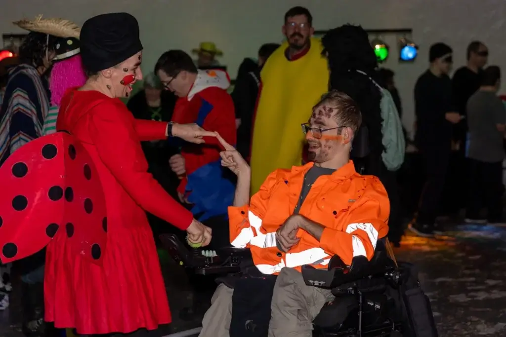 Verkleidete Personen tanzen an der Fasnacht, Marienkaefer-Kostuem trifft Rollstuhlfahrer