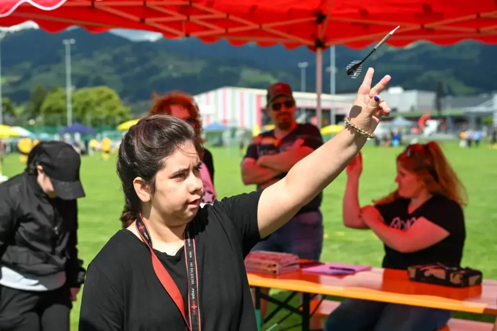 Junge Frau wirft konzentriert einen Dartpfeil beim Rhyboot-Sportanlass im Freien