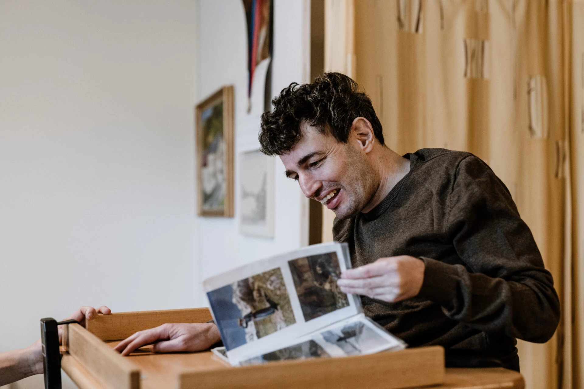 Junger Mann betrachtet freudig Fotos an einem Holztisch im Wohnbereich