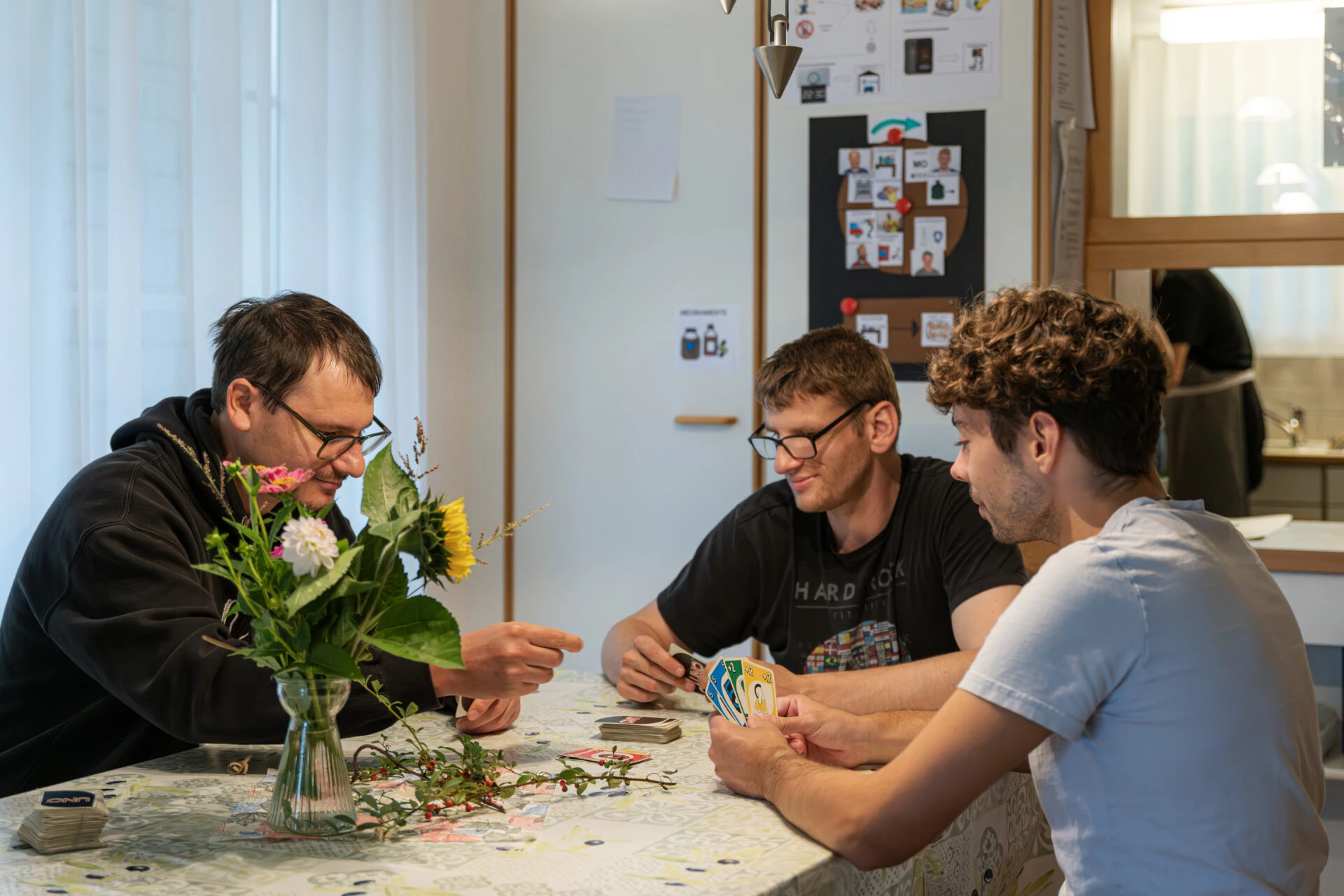 Drei Bewohner spielen gemeinsam Karten an einem Tisch in der Wohngruppe