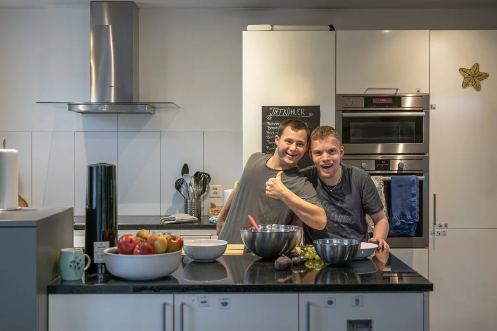 Zwei junge Maenner stehen lachend zusammen in der Kueche und bereiten Essen zu