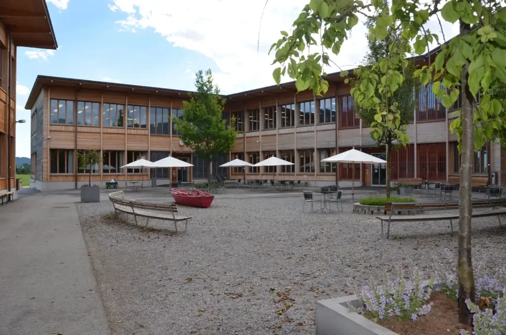 Innenhof des Rhyboot-Gebaeudes mit Sitzbaenken, Sonnenschirmen und modernem Holzbau
