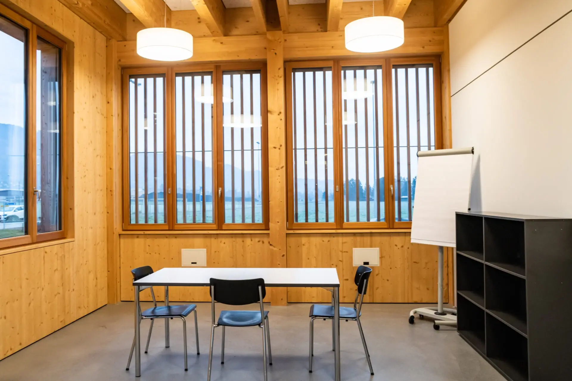 Kleines Sitzungszimmer A3 mit Tisch, Stuehlen und Flipchart in hellem Holzbau