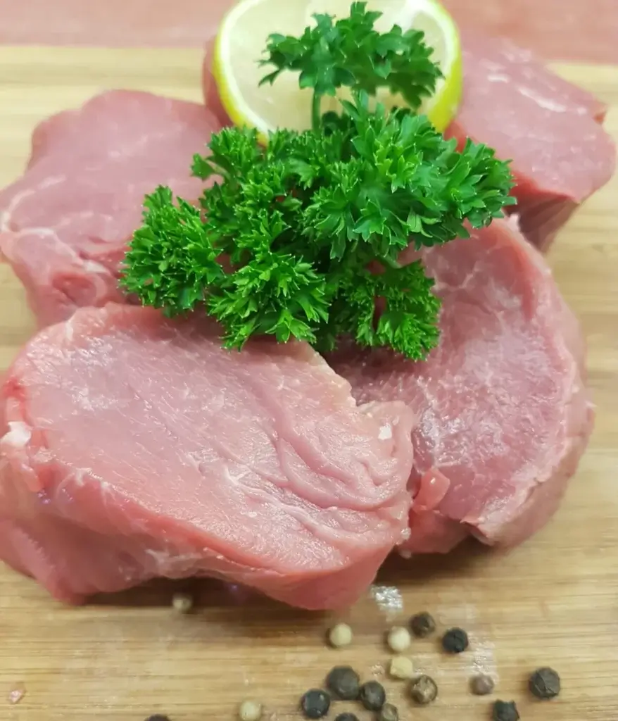Rohes Kalbsfilet auf Holzbrett garniert mit Petersilie, Zitrone und Pfefferkoernern