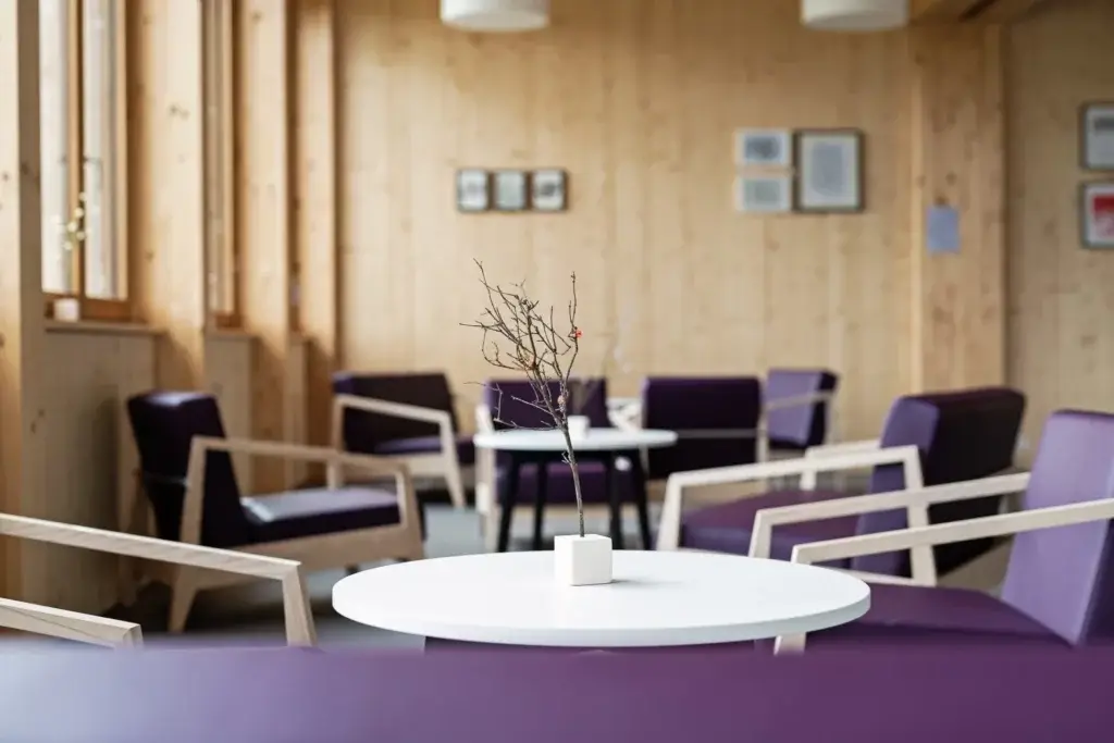 Gemuetliche Lounge mit violetten Sesseln, runden Tischen und warmer Holzatmosphaere