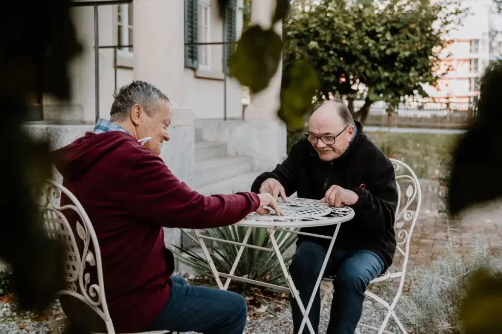 Zwei Bewohner spielen gemeinsam ein Puzzle im Garten vor dem Pfortenhaus