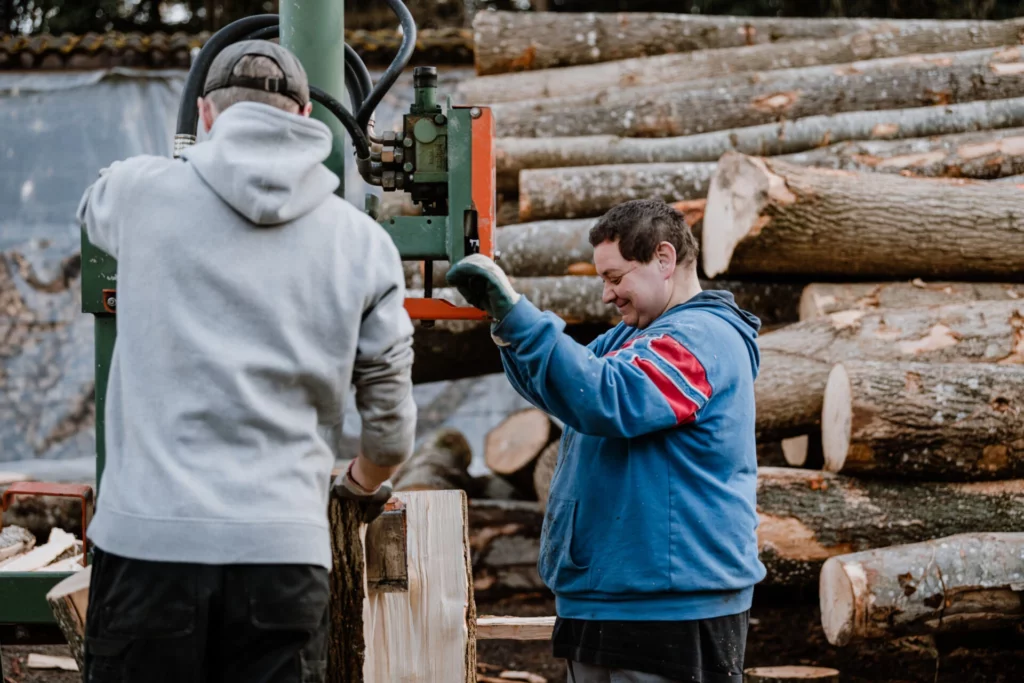 Zwei Mitarbeiter spalten gemeinsam Holz an einer Holzspaltmaschine im Freien