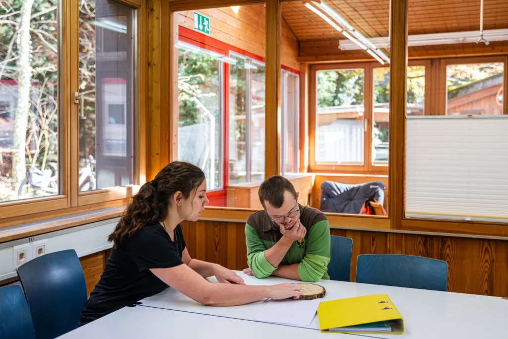 Betreuerin und Bewohner besprechen gemeinsam Unterlagen im hellen Sitzungsraum