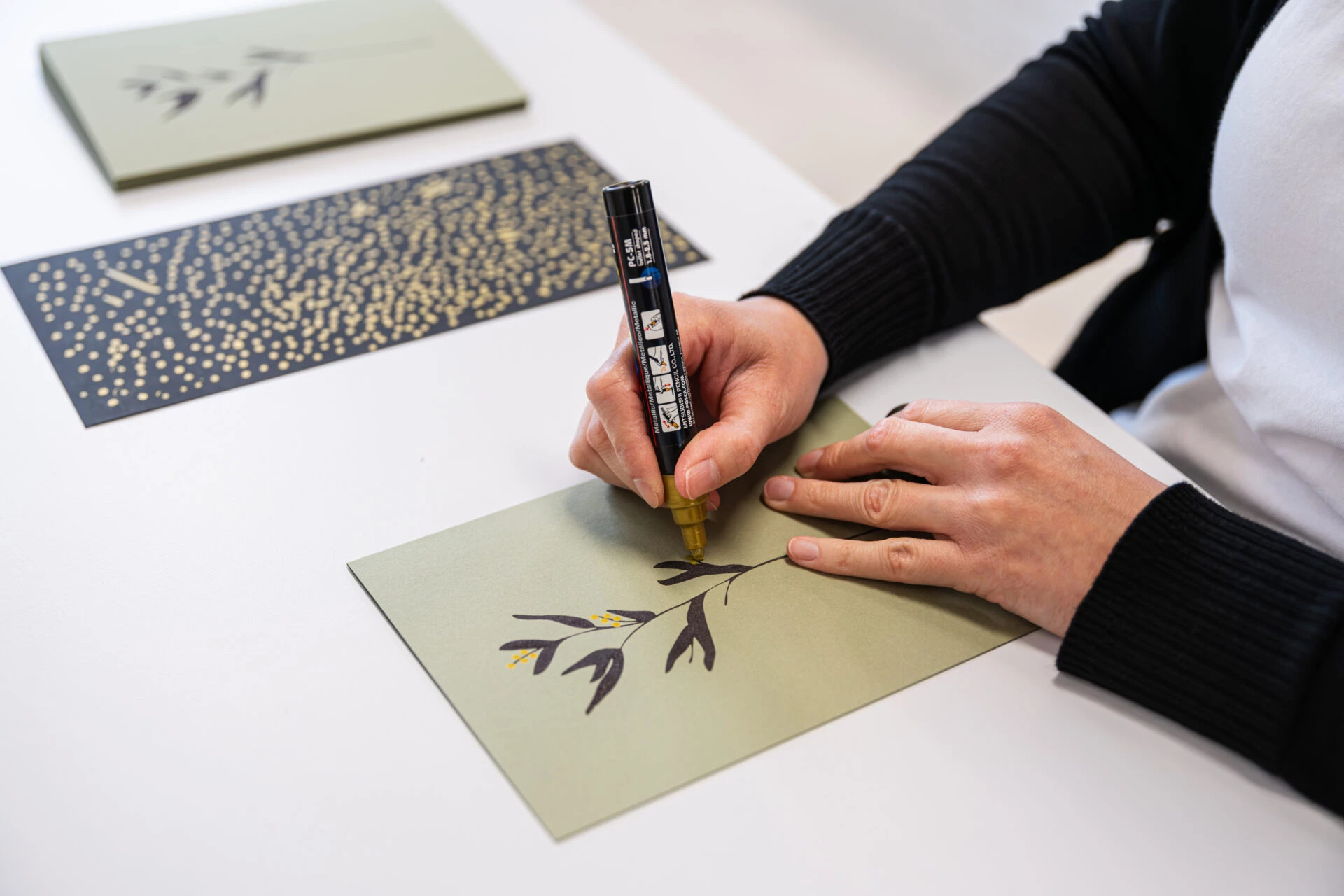 Haende bemalen eine Karte mit Pflanzenmotiv mit einem goldenen Stift