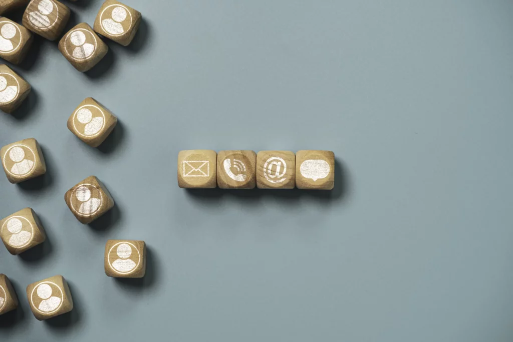 Holzwuerfel mit Kontakt-Symbolen: Brief, Telefon, E-Mail und Personen-Icons