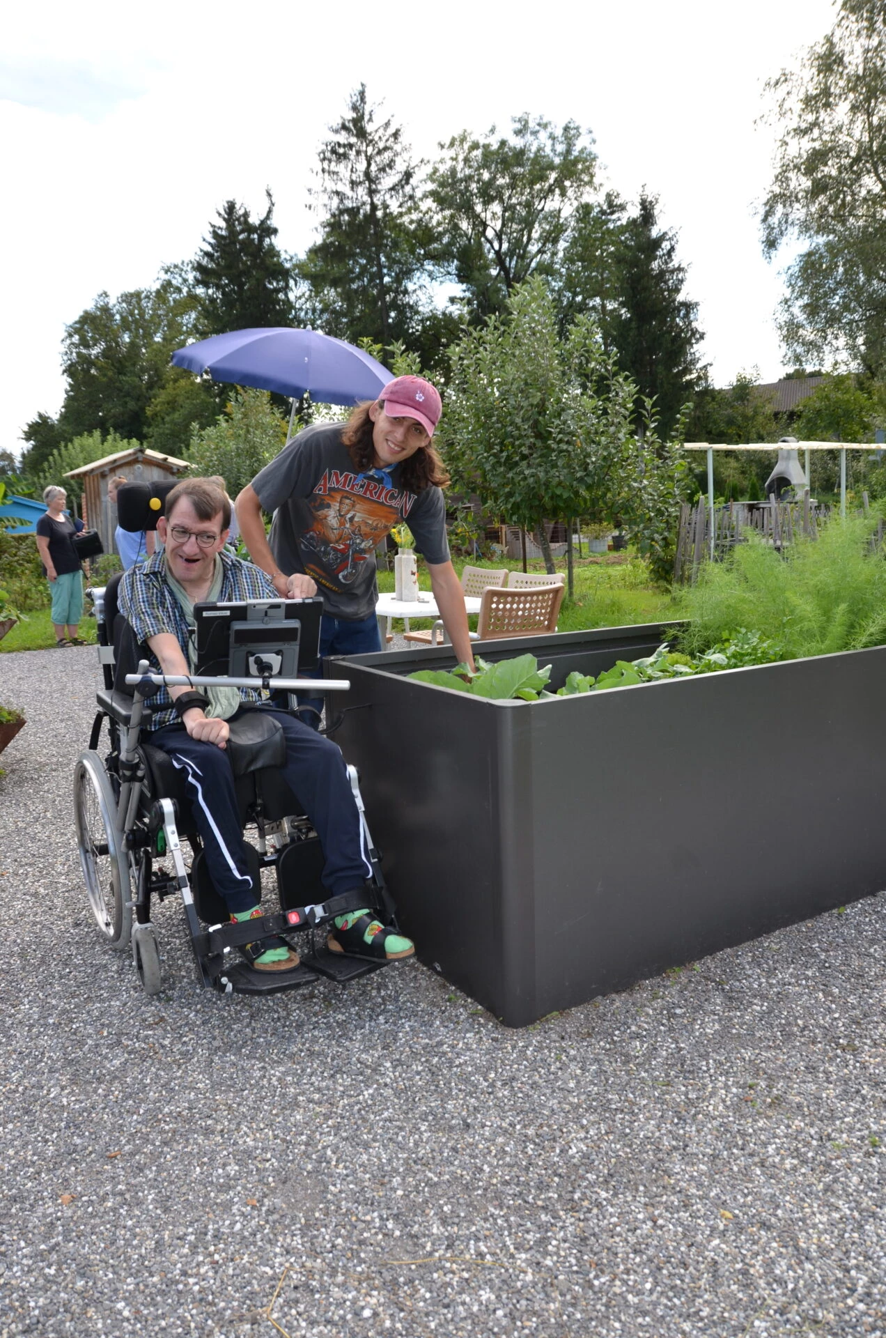 Bewohner im Rollstuhl und Betreuerin am rollstuhlgerechten Hochbeet im Schrebergarten