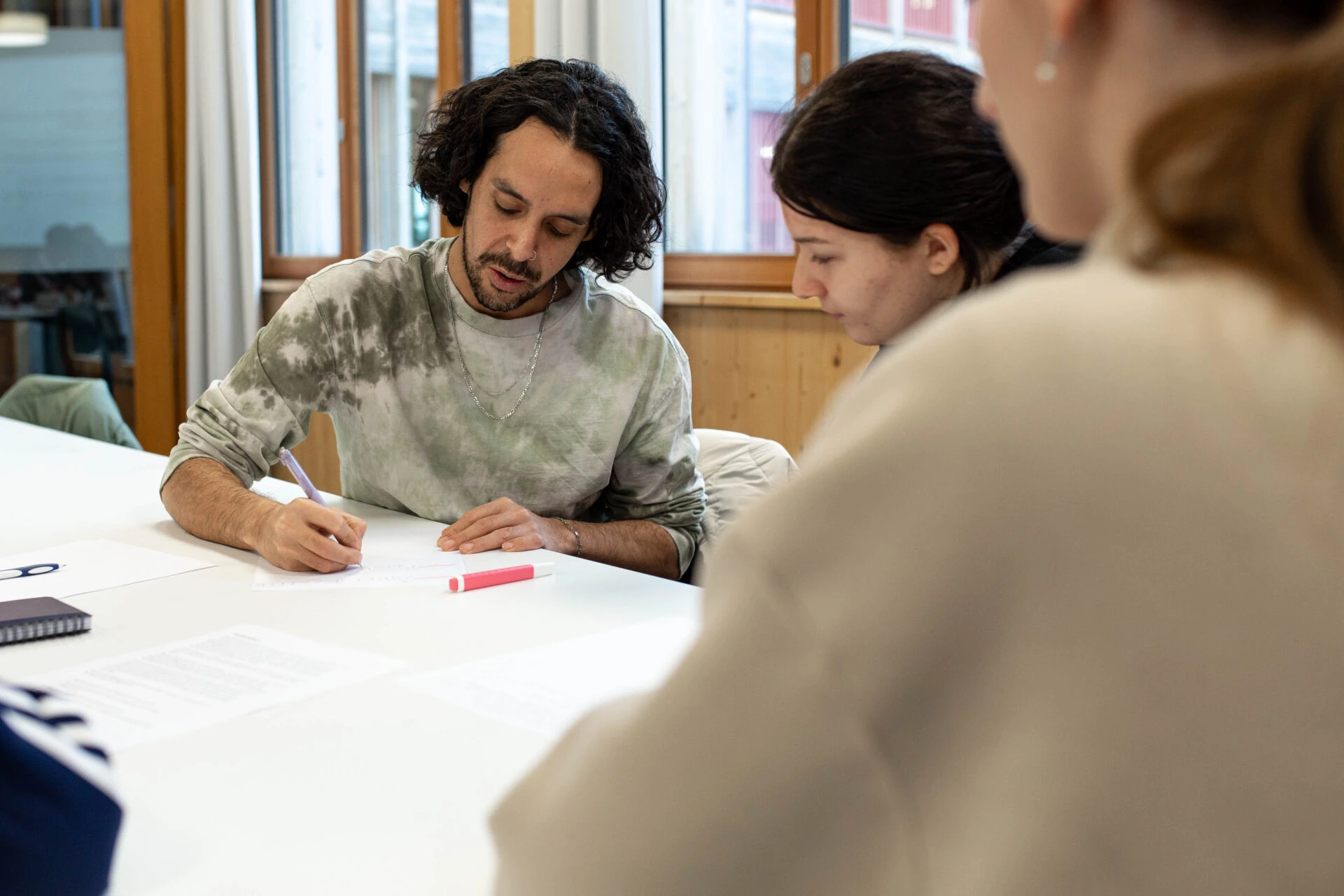 Junge Personen arbeiten konzentriert mit Stift und Papier an einem Tisch in der Ausbildung